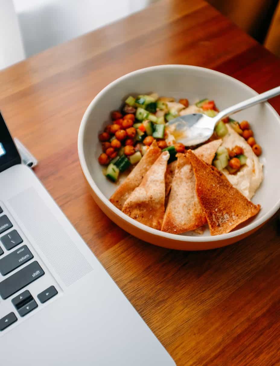 Bowl of food sitting on a desk with a computer next to it.